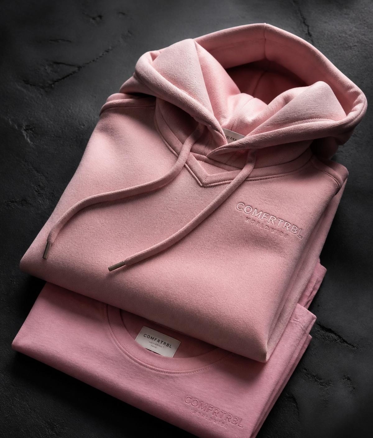 Folded pink heavyweight hoodie with tonal embossed logo over a matching tee